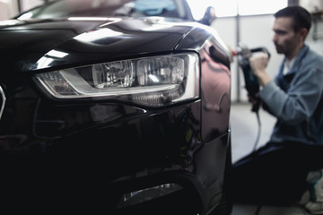 Fototapeta premium Car detailing - Hands with orbital polisher in auto repair shop. Selective focus.