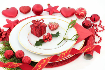Christmas dinner table setting with porcelain plates, holly, mistletoe and fir, red bauble decorations and decorative ribbon on white background