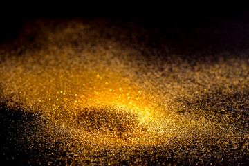 Fototapeta na wymiar Sprinkle glitter gold dust on a black background with copy space