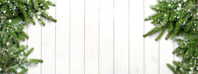 Christmas snow-covered branches on a white wooden background. New Year's background, holiday, christmas, snow, winter, green branches top view with copy space. Long format.