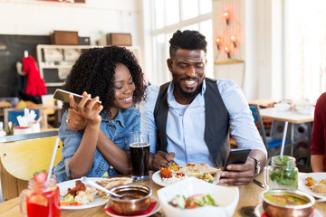 happy man and woman with smartphones at restaurant