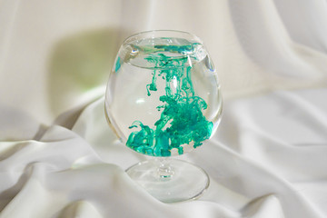 Green watercolor in a glass. Color mix in the glass. Oil paint in water. Colorful cocktail. The initial stage of mixing.