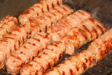 Close-up of traditional romanian barbecue raw meat (mici, mititei) on hot grill with smoke, selective focus