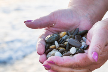 Sea stones in hands on the beach at sunset