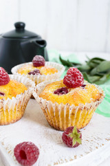 Delicious freshly baked muffins with raspberries, decorated with powdered sugar, teapot on a white wooden background.