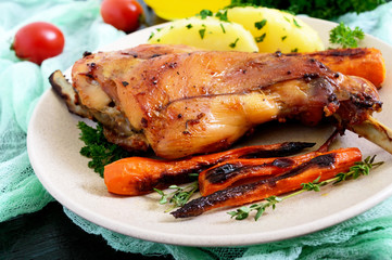Fried rabbit leg, garnish of boiled potatoes, grilled carrots - on a plate on a dark background.