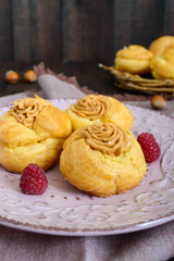 Delicious profiteroles with caramel nut cream on a ceramic plate on a dark wooden background.