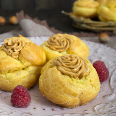 Delicious profiteroles with caramel nut cream on a ceramic plate on a dark wooden background.
