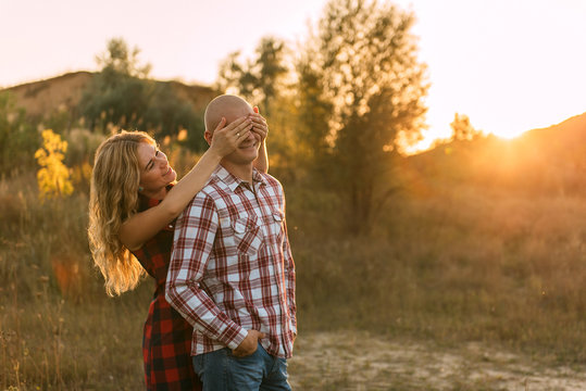 man guy in plaid shirt and woman girl in red checkered dress kiss standing in grass sitting in grass half on top on sunset background