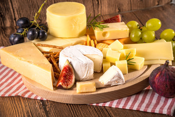 Assorted cheeses on round wooden board plate. Camembert cheese, cheese grated bark of oak, hard cheese slices, walnuts, grapes, crackers, bread, figs