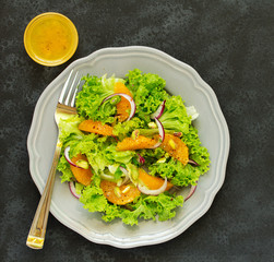 A plate of lettuce, with slices of orange, red onion, with vinaigrette dressing.