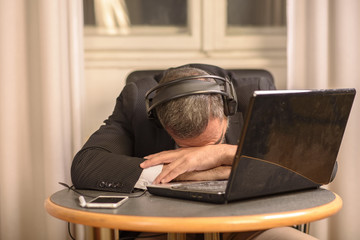 Senior business man sleeping on his laptop with his headphones on, listening to music or a hypnosis...