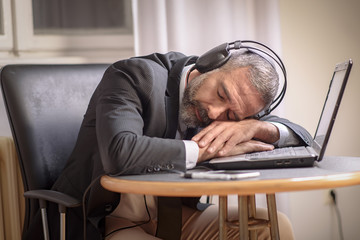 Senior business man sleeping on his laptop with his headphones on, listening to music or a hypnosis...