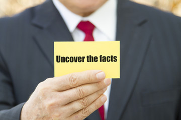 Businessman showing a card with text UNCOVER THE FACTS