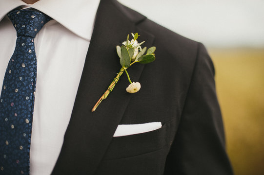 Groom wearing patterned navy tie and black suit with diy simple broken flower boutonniere