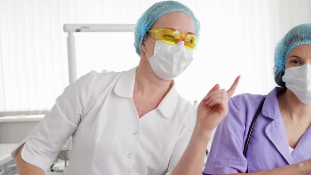 Two silly funny female doctors in medical masks and caps dancing in hospital room. Enjoying themselves having fun during break. Medical professional staff relaxing