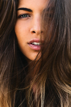 Closeup portrait of a young brunette woman with long hair looking at camera.
