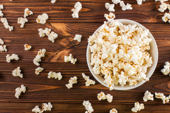 Popcorn horizontal banner. Red stripped paper cup and kernels lying on dark brown wooden background. Copy space. Top view.