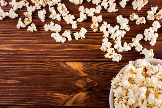 Popcorn horizontal banner. Red stripped paper cup and kernels lying on dark brown wooden background. Copy space. Top view.