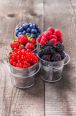Berries colorful assortment blueberry, raspberry, red currant, strawberry, in five old tin cans on rustic wooden table in studio
