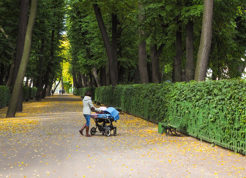 Young girl-mother walking with twins in a stroller in the autumn. 
