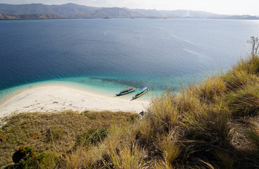 Top view of two boats at the coast of a white sand beach surrounded by  blue turquoise colored ocean water in Flores Indonesia.