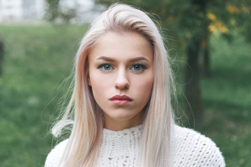 Portrait of natural beautiful blonde girl in a white knitted sweater.