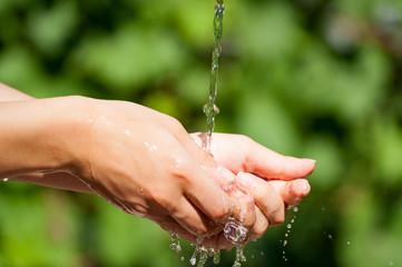 Woman washing hand outdoors. Natural drinking water in the palm. Young hands with water splash, selective focus