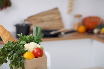Paper bag full of vegetables on the table in kitchen interiors. Healthy meal and vegetarian concept