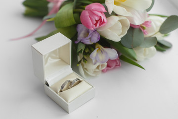 Obraz na płótnie Canvas delicate flower arrangement and wedding rings. gold wedding rings in white box and a bridal bouquet with space for text. white gold wedding rings and pink flowers isolated in white background
