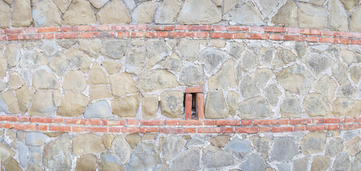 Panoramica di un muro in pietra con decorazione orizzontale fatta con mattoni rossi.