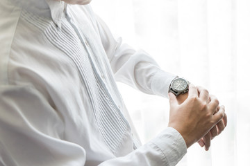 Close up of businessman wearing wristwatch on his hand checking time or morning wedding preparation