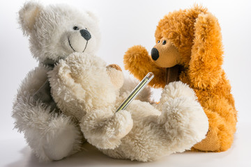Three teddy bears, one has a medical thermometer on white background.