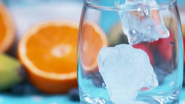 Slow motion water and ice cubes poured into a glass on colorful breakfast table