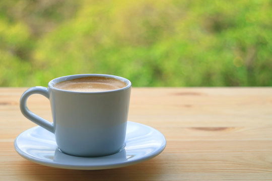 One Cup of Hot Coffee on the Wooden Table of Outdoor Seating, Blurred Green Bush in Background 