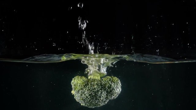 broccoli falling in the water on black background