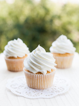 White vanilla cupcakes on a wooden table and blurred green background. Bright and shine photo
