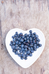 Fresh forest blueberries in heart plate on wooden background autumn