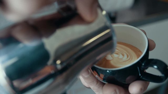  Close up hands of barista preparing coffee & creating pattern in the froth