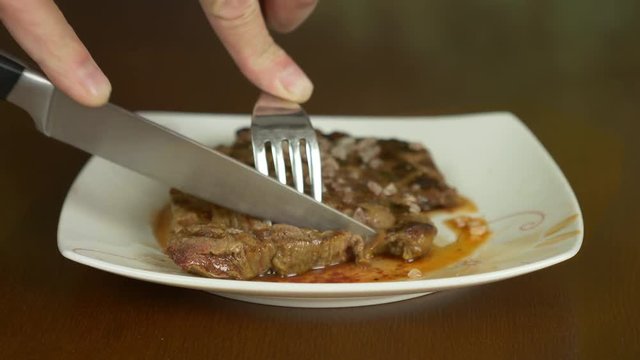 Close up locked shot of steak. Hands with knife and fork take part of meat steak from plate.