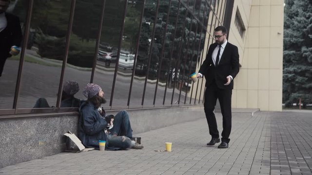 The businessman banishes the bearded homeless man and throws back his cup with coins.