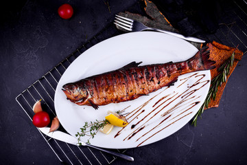 whole grilled fish on a white plate and black background