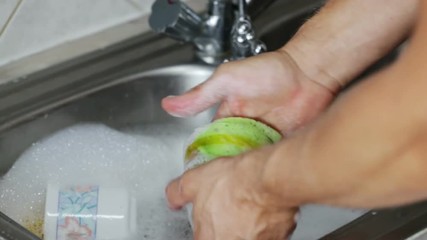 Man washes the dishes, glass, mug., with foam. Closeup.
