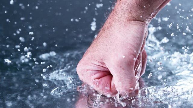  Clenched fist punching wet surface with water spray, close up & slow motion