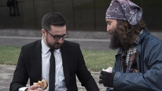Smiling businessman sharing food with cheerful homeless on city street.