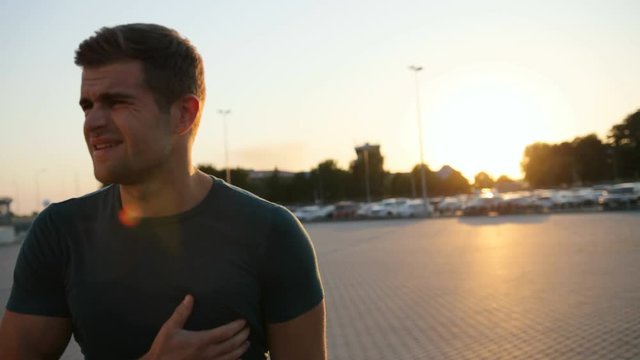 Closeup. Portrait of a young runner. He pulls off the headphones and feels the pain in his chest. Touching his chest. Emotions full of pain. Blurred background