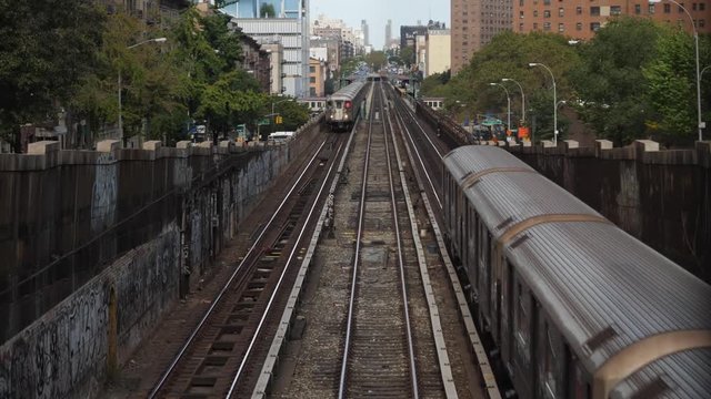 Two Harlem bound subway trains pass each other in upper Manhattan on an elevated track on Broadway on a summer day.  	