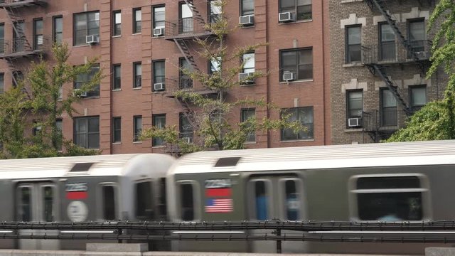 Two New York City subway trains pass by Harlem apartment buildings on an elevated track.  	