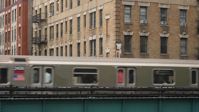 A New York City subway train passes by Harlem apartment buildings and a corner liquor store on an elevated track.  	