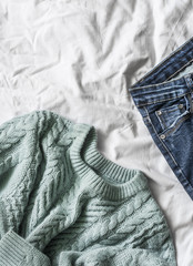 Women's blue knitted sweater and jeans on the bed, top view. Free space for text